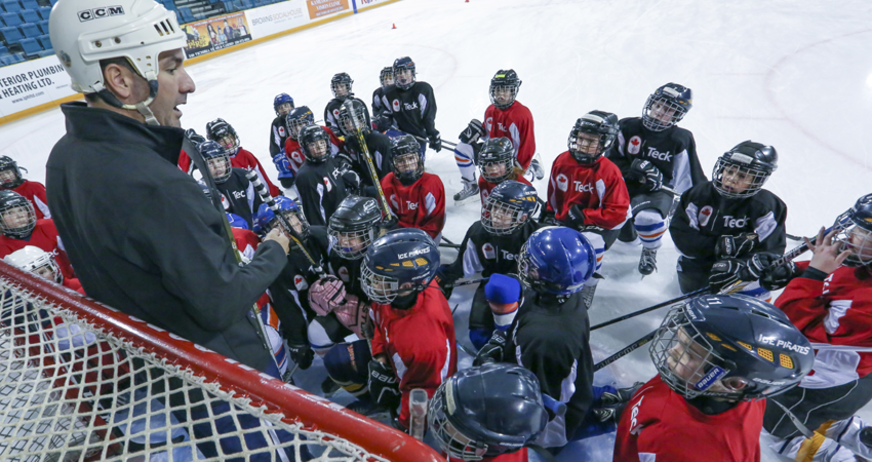 Hockey coach talking to a group of young players on the ice, as they gather closely around him.